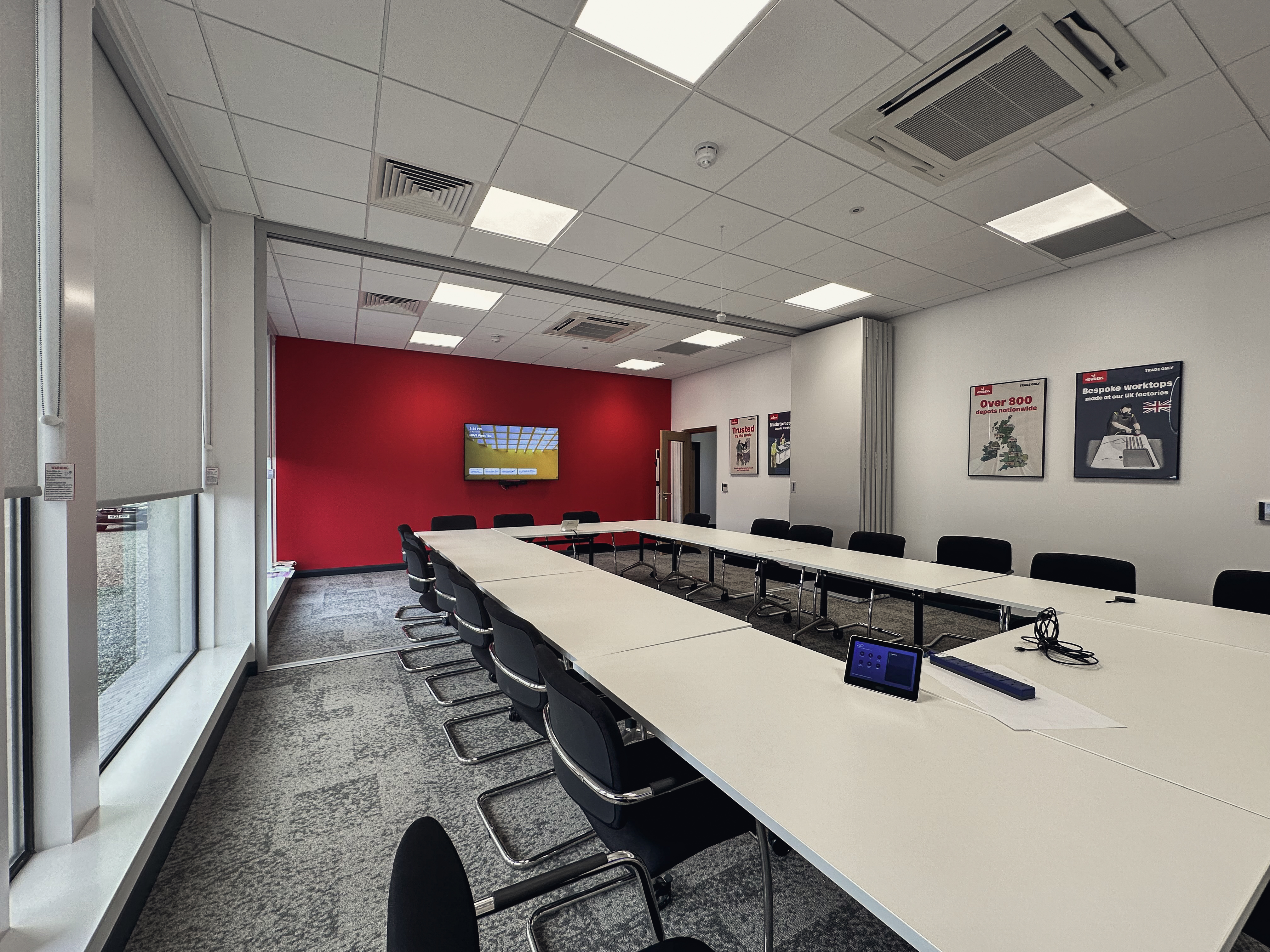 Branded interior detail of a Howdens fit-out: warm timber panelling with signature Howdens red joinery and seating