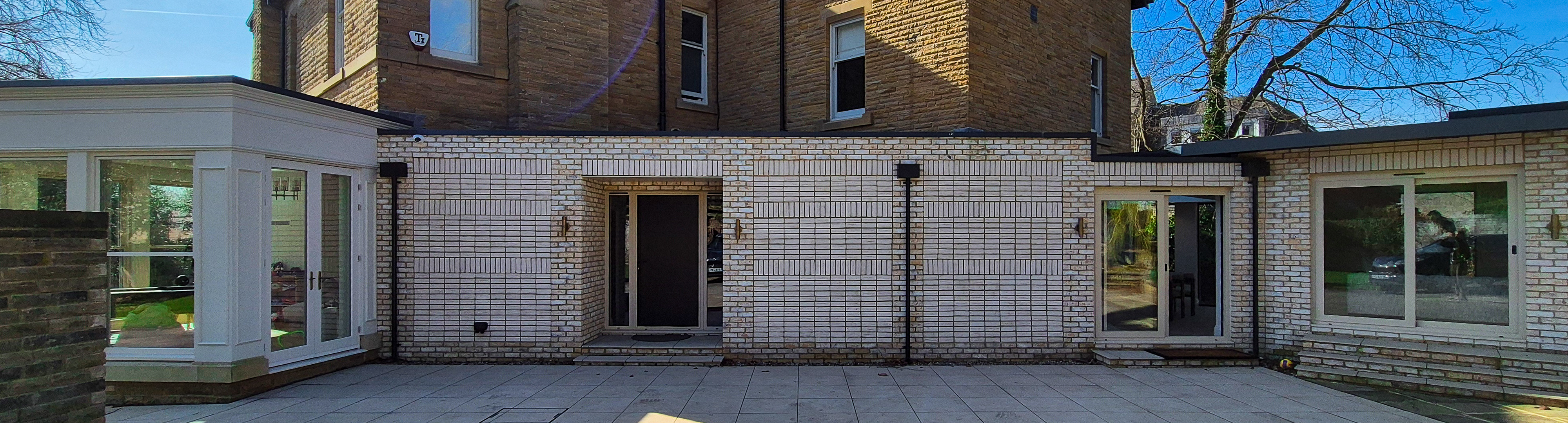 Garden pavilion extension in Roundhay, Leeds — white-brick single-storey wings framing a paved courtyard behind a sandstone Victorian villa, by we are _