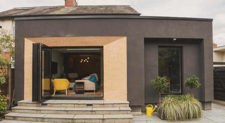 Contemporary rear extension in Roundhay, Leeds, with dark textured render and apricot Tiles of Stow surround framing black bifold doors, by we are _